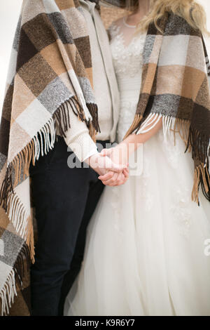 Liebe, Engagement, Atmosphäre. Es ist ein süßes Paar der Jungvermählten in Hochzeit Kostüme gekleidet und bis in den gemütlichen Plaid mit Fransen verpackt, Sie halten sich an den Händen der jeweils anderen Stockfoto