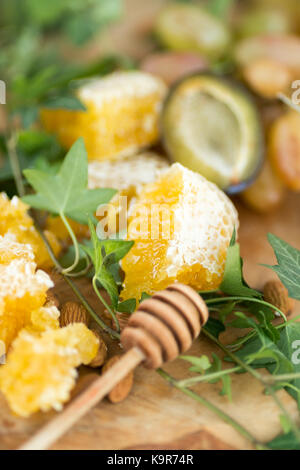 Essen, Behandlung, gesunde Ernährung Konzept. In der Nähe von frisch und saftig Gelbe honeycombes Orte in der Nähe von grünen Blättern des wilden Wein und Löffel aus Holz, spezielle für Honig Stockfoto