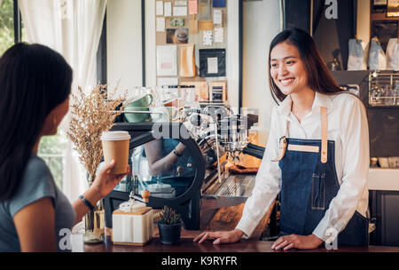 Asiatische Frau barista Schürze tragen Jean serviert Kaffee Tasse zu Kunden an Theke mit Smile Emotion zu gehen, Cafe Restaurant Service Konzept, Inhaber klein Stockfoto