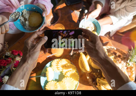 Top Betrachtungswinkel der männlichen Händen unter Foto von Frühstückstisch mit frischen Früchten und Müsli Brei Stockfoto