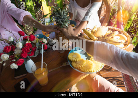 Gruppe der Unkenntlich Leute beim Frühstück Tabelle Holding Ananas in die Hände junger Mann und Frau in Morgen Essen frische Früchte Stockfoto