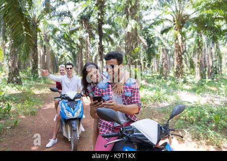 Junge Menschen gehen verloren und die Verwendung von Smart Phone GPS-Karte während der Fahrt auf Roller zwei fröhliche Paare auf dem Fahrrad in den tropischen Wald Stockfoto