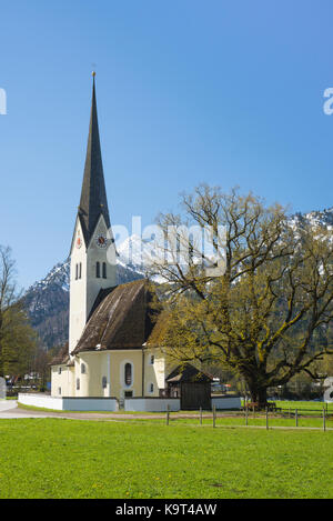 Die Kirche von St. Leonhard am Schliersee vor schneebedeckten Bergen und spriessen die Blätter auf den Bäumen im Frühjahr Sonnenlicht, Bayern Deutschland Stockfoto