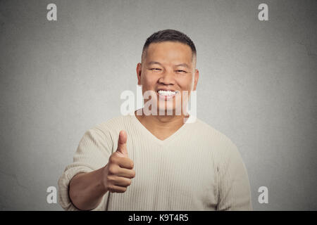 Nahaufnahme Porträt glücklich gut aussehend junge lächelnde Mann Mitarbeiter geben Daumen nach oben Zeichen Geste an Kamera isoliert grauen Wand Hintergrund. Positive menschliche Emoti Stockfoto