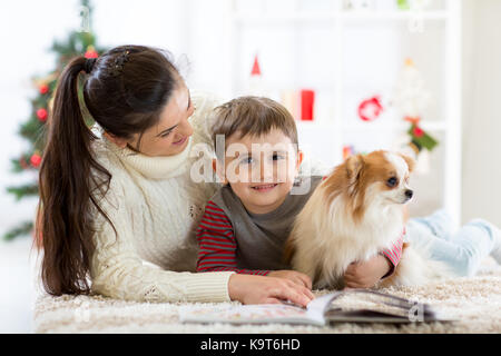 Glückliche Familie und der Hund Ausgaben zusammen Weihnachten zu Hause in der Nähe der Weihnachtsbaum. Neues Jahr Konzept Stockfoto