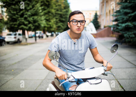 Fröhlichen junger Mann im Helm reitet auf Roller in der Stadt. Stockfoto