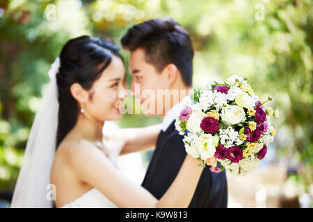 Junge asiatische frisch vermählte Paar umarmen während der Trauung, auf dem Blumenstrauß konzentrieren. Stockfoto