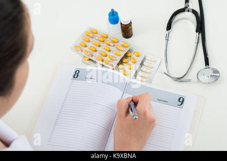 In der Nähe der weiblichen Arzt im Buch schreiben am Schreibtisch Stockfoto