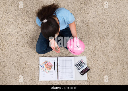 Frau sitzt auf dem Teppich mit Rechnungen und Geld im Sparschwein Münze einfügen Stockfoto