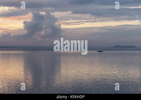 Ein See in der Abenddämmerung, mit schönen Wolken Reflexionen und ein entfernter Fischer auf einem kleinen Boot Stockfoto