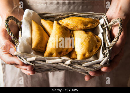 Junge Frau mit in den Händen Weidenkorb mit frisch gebackenen empanadas Umsatz Torten mit Gemüse Käse in Tomatensauce. Knfolk Stil. Gemütliche authe Stockfoto