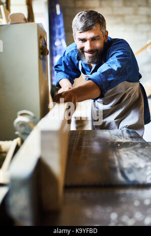 Portrait von qualifizierten bärtigen Carpenter lächelte glücklich beim Arbeiten mit Holz in tischlerarbeiten Shop Stockfoto