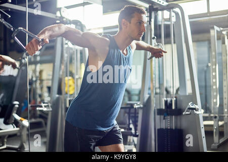 Junge sportliche Mann mit Kabel crossover Maschine während Sie intensives Training, Interieur des modernen Fitnessraum auf Hintergrund
