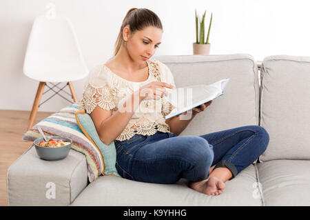 Schöne Frau zu Hause sitzen auf der Couch und liest ein Buch Stockfoto