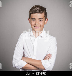 Closeup Portrait zuversichtlich gut aussehender Teenager, jungen Mann im weißen Hemd lächelnd, glücklich, die Arme verschränkt graue Wand Hintergrund isoliert. Positive menschliche Gesicht Stockfoto