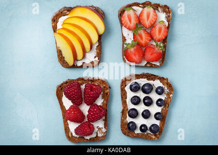 Diät Frühstück. Toast mit Frischkäse und frischen Beeren und Früchte: Bananen, Himbeere, Heidelbeere, Erdbeere, Pfirsich. Ansicht von oben Stockfoto