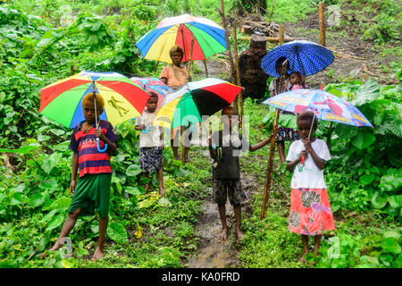 Einheimische Frauen mit Kindern mit bunten Sonnenschirmen im Regen in das Dorf Rangsuksuk, Insel von Pfingsten, Vanuatu Stockfoto