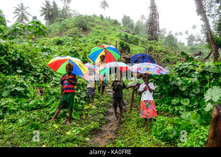 Einheimische Frauen mit Kindern mit bunten Sonnenschirmen im Regen in das Dorf Rangsuksuk, Insel von Pfingsten, Vanuatu Stockfoto