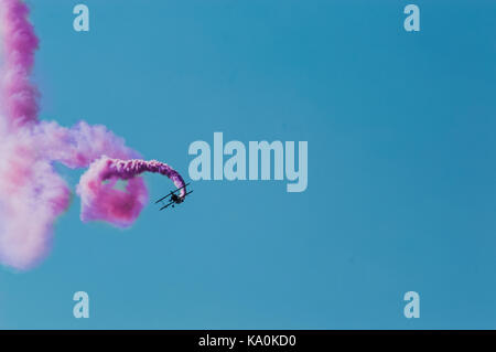Aerobatic Flugzeug verlassen ein rosa Rauch Trail in den strahlend blauen Himmel. Stockfoto