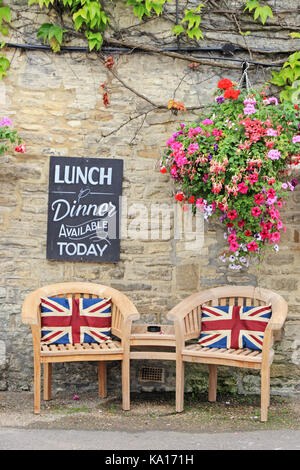 Hölzerne Stühle und Tisch mit Union Jack Kissen außerhalb Cotswolds Public House. Stockfoto