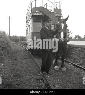 1950, historisch, draußen auf einer Schiene stehend, ein uniformierte Dirigent mit einer Pferdebahn neben dem Bahnsteig in Fintona, Nordirland, Großbritannien. Ein beliebtes Massenverkehrsmittel Ende des 19. Jahrhunderts wurden die von Pferden gezogenen Straßenbahnen zurückgezogen, als sie zuerst Dampf abnahmen und dann die elektrischen Straßenbahnen übernahmen. Diese Pferdestraßenbahn in Fintona, Grafschaft TRYONE, war die letzte in Irland, die noch in Betrieb war, schloss aber 1957 nach 104 Jahren zusammen mit den beiden Bahnhöfen Fintona und Fintona Junction, die die Straßenbahn miteinander verband. Stockfoto