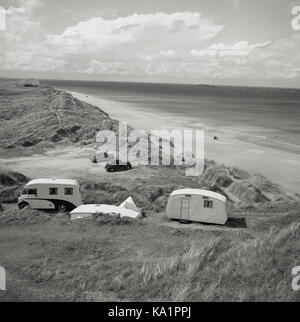 1950, historisch, ein Wohnmobil und Wohnwagen der damaligen Zeit, geparkt auf Sanddünen mit Blick auf einen langen Sandstrand und die Küste, Antrim, Nordirland. Stockfoto