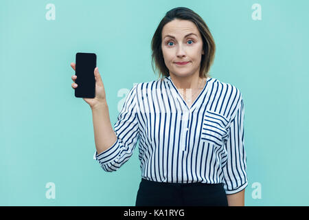 Erfolg Business Frau zeigt neue Smartphone und Blick auf Kamera. Außenaufnahme, blauer Hintergrund Stockfoto