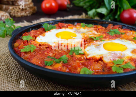 Shakshuka - eine Schale der Eier in einer Sauce aus Tomaten gebraten, Paprika, Zwiebeln und Gewürze. Israelische Küche. Für das Frühstück mit Roggenbrot serviert. Stockfoto