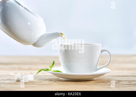 Schale mit grünem Tee und Teekanne auf weiße Holztisch Hintergrund Stockfoto