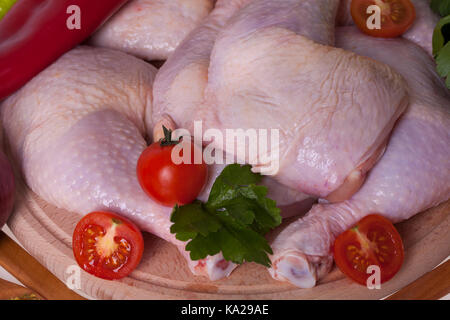 Schließen Sie frisches Huhn Oberschenkel und Unterschenkel auf einem Holzbrett mit Gemüse - Kirsche Stockfoto