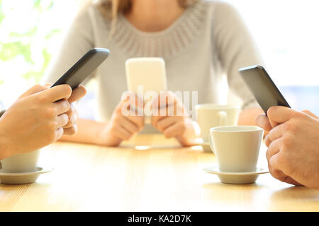 Schließen Sie bis zu drei Freunde die Hände über ihre Smartphones sitzen in einer Bar oder einem Home Interior Stockfoto