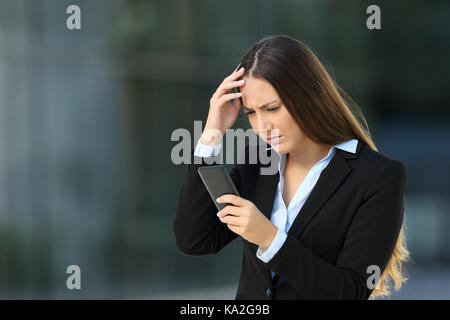 Besorgt executive Lesen schlechte Nachrichten in ein Handy auf der Straße mit einem Bürogebäude im Hintergrund Stockfoto