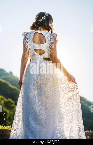 Braut im Brautkleid mit Blick auf den Sonnenuntergang zurück lit Stockfoto