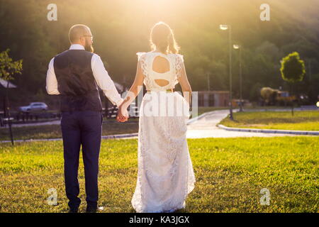 Braut und Bräutigam in Richtung Sonnenuntergang halten sich an den Händen Stockfoto