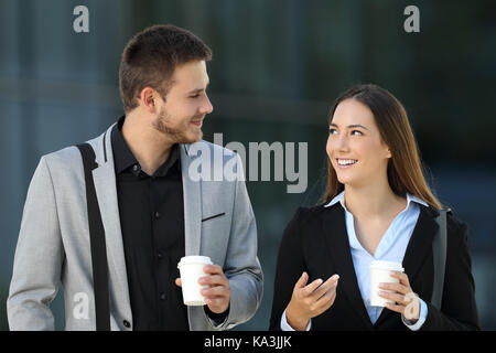 Von vorne: Ein glückliches Paar von Führungskräften zu Fuß und im Gespräch auf der Straße mit einem Bürogebäude im Hintergrund Stockfoto