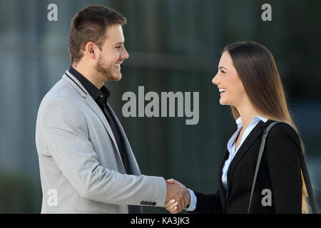 Seitliche Sicht auf zwei Glückliche Führungskräfte treffen und Handshake auf der Straße mit einem Bürogebäude im Hintergrund Stockfoto