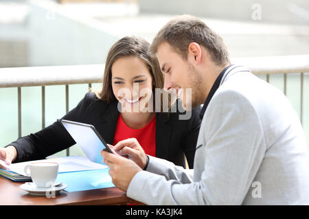 Zwei Führungskräfte Beratung online Daten in einer Tablette in einem Restaurant Terrasse sitzen Stockfoto