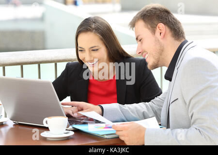 Zwei Führungskräfte arbeiten auf der Linie mit einem Laptop in einer Bar auf der Terrasse sitzen Stockfoto