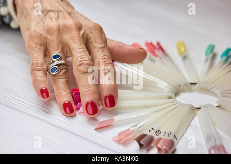 Womans gepflegten Hand mit Silber Ring. Alte Frau mit schönen roten Maniküre tragen Luxus Ring. Elegante Maniküre der älteren Frau. Stockfoto