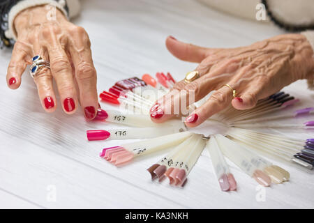 Senior womans Hände mit roten Maniküre. Schöne alte Frau Hände mit perfekter Rote nägel Auswahl Sommer rosa Nagel Sample. Stockfoto