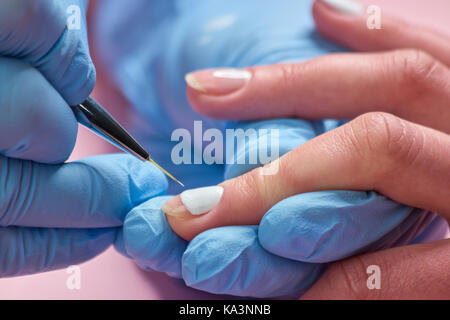 Maniküre, Nail Design für den Kunden. Weibliche Hände in blau Handschuhe Anwendung Nagellack auf gesunden womans Hand. Nagelpflege und Maniküre. Stockfoto
