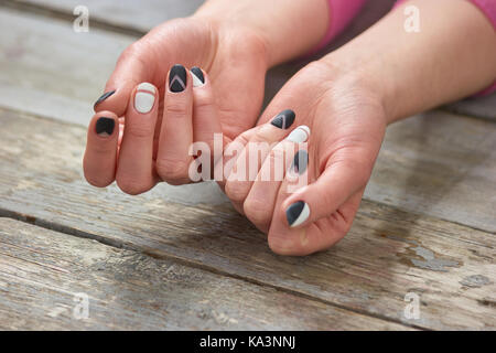 Weiblich gepflegte Hände auf Holz- Hintergrund. Frau Hände mit Schwarz und Weiß Matte Nägel auf alten vintage Hintergrund. Nail Salon und Spa. Stockfoto