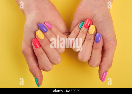 Weibliche Nägel lackiert in verschiedenen Farben. Womans Nägel mit multicolor polnischen auf gelbem Hintergrund, Ansicht von oben. Stockfoto