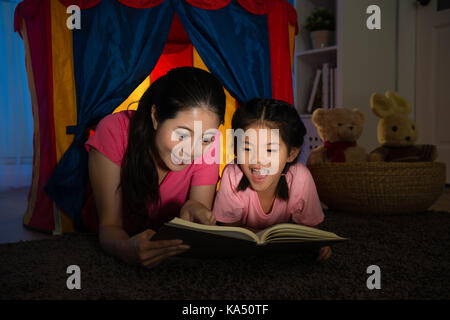 Schönheit und Glücklich lächelnde Dame hübsches kleines Mädchen lesen Bedtime Story Book in Kinderspielzeug Zelt liegen glücklich zusammen genießen Nacht Schlafzimmer. Stockfoto