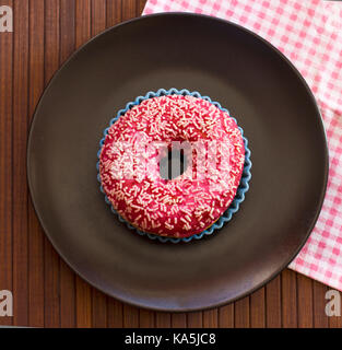 Hell rosa Donut auf braunem Holz- Hintergrund. Mit rosa-karierten Tuch Stockfoto