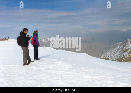 Zwei Wanderer genießen Sie den Blick vom Gipfel des Helvellyn im späten Winter Schnee, Lake District, Cumbria, Großbritannien Stockfoto