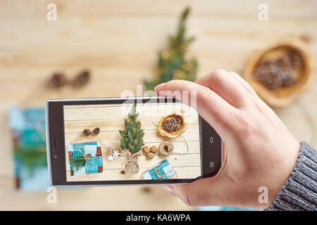 Woman's Hand unter Foto von Weihnachtsschmuck und Geschenke von Smartphone Stockfoto