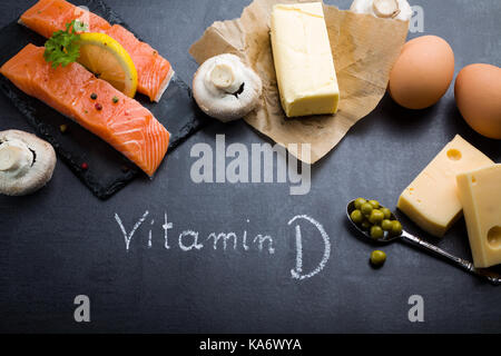 Schwarzer Schiefer Tisch mit Produkt reich an Vitamin D und Omega 3. Wort Vitamin D durch weiße Kreide geschrieben. Stockfoto