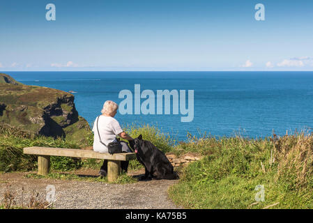 Küste von North Cornwall - eine Frau sitzen auf einer Bank mit ihrem Hund auf den Klippen in Cornwall. Stockfoto