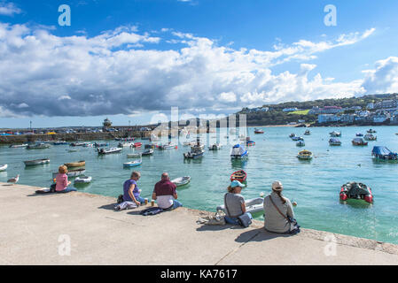 St Ives - Urlauber entspannen am Kai und genießen den Blick über den Hafen von St Ives in Cornwall. Stockfoto